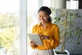 Happy black female entrepreneur using tablet standing near window at modern coworking office, copy space Royalty Free Stock Photo