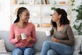 Happy black girlfriends enjoying weekend together, drinking coffee on couch