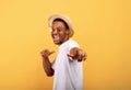 Happy black guy in casual summer outfit, straw hat and sunglasses pointing at you on yellow studio background Royalty Free Stock Photo