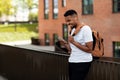 Happy black guy with smartphone listening to music in earbuds, standing outdoors in urban area in the city Royalty Free Stock Photo