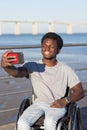 Happy Black guy in wheelchair taking selfie on his mobile phone