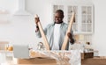 Happy black handyman assembling new wooden table, looking at laptop at online instructions in kitchen interior, panorama Royalty Free Stock Photo