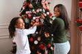 Happy black woman and girl decorating Xmas tree, looking back Royalty Free Stock Photo