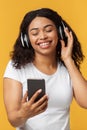 Happy black lady enjoying newest stereo headset and mobile music app, listening to music over yellow studio background Royalty Free Stock Photo