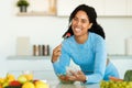 Happy black lady in sportswear eating salad at home in kitchen, leaning on table and using smartphone, free space Royalty Free Stock Photo