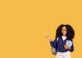 Happy black lady student in glasses, with backpack and copybooks, pointing aside at free space, on yellow background Royalty Free Stock Photo