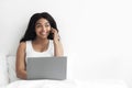 Happy black lady talking on cellphone and using laptop, confirming her order on phone, sitting on bed, empty space Royalty Free Stock Photo