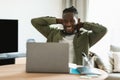 Happy black male freelancer looking at laptop computer and relaxing, holding hands behind head, sitting at desk at home Royalty Free Stock Photo