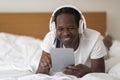 Happy Black Man With Digital Tablet And Wireless Headphones Relaxing In Bed Royalty Free Stock Photo
