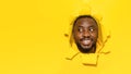 Happy black man looking aside at free space and smiling, noticing something interesting, yellow paper hole Royalty Free Stock Photo