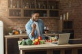 Happy black man looking at laptop and cooking dinner Royalty Free Stock Photo