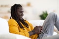 Happy black man messaging on smartphone while relaxing on couch at home Royalty Free Stock Photo