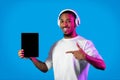 Happy black man showing digital tablet with mockup, using headphones Royalty Free Stock Photo