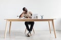 Happy black man sitting at desk with laptop, daydreaming, taking break from online work against white studio wall Royalty Free Stock Photo