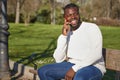 Happy black man talking on smart phone sitting in a park on a sunny day. Royalty Free Stock Photo