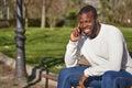 Happy black man talking on smart phone sitting in a park on a sunny day. Royalty Free Stock Photo
