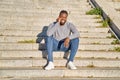 Happy black man talking on smart phone sitting on stairs. Young man in jeans and grey sweater. Concept of communication Royalty Free Stock Photo