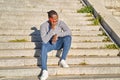 Happy black man talking on smart phone sitting on stairs. Young man in jeans and grey sweater. Concept of communication Royalty Free Stock Photo