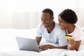 Happy black man and woman using laptop in bed, shopping Royalty Free Stock Photo
