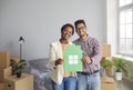 Happy young black couple standing in their new home, holding paper house and smiling Royalty Free Stock Photo