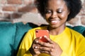 Happy Black millennial young woman using cellphone, typing message, taking in social networks