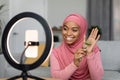 Happy black muslim blogger lady making review of stone roller and filming video on smartphone set on ring lamp Royalty Free Stock Photo