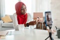 Happy black muslim female blogger showing makeup product to cellphone camera, making video with cosmetics at home Royalty Free Stock Photo