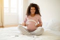 Happy black pregnant woman holding headphones near belly, playing melody to baby Royalty Free Stock Photo