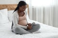 Happy black pregnant woman with ultrasound picture of baby sitting on bed