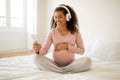 Happy black pregnant woman wearing headphones using smartphone at home Royalty Free Stock Photo