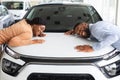 Happy Black Spouses Hugging Hood Of Their New Car In Dealership Office