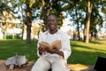 Happy black student guy reading interesting book, having rest after classes in park, sitting on bench on sunny day Royalty Free Stock Photo