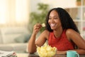 Happy black woman eating potato chips at home