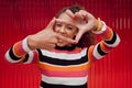 Happy, black woman and finger frame over eyes for funny face expression on red background. Fashion, comic and positive