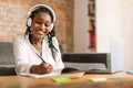 Happy black woman in headphones studing online with laptop from home, watching webinar and taking notes to notepad Royalty Free Stock Photo