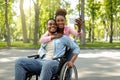 Happy black woman and her impaired boyfriend in wheelchair taking selfie together, hugging at city park Royalty Free Stock Photo