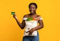 Happy black woman holding shopping bag with groceries and showing credit card Royalty Free Stock Photo