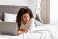 Happy black woman lying in bed reading text message Royalty Free Stock Photo