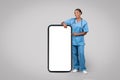 Happy black woman nurse in blue uniform near big smartphone with empty screen Royalty Free Stock Photo