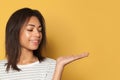 Happy black woman showing empty open hand for advertising marketing or product placement on yellow background