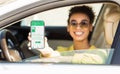 Happy black woman showing smartphone with mobile app to purchase eco fuel from her car window, panorama