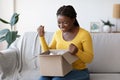Happy black woman unboxing parcel at home, emotionally reacting to successful shopping Royalty Free Stock Photo