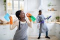 Happy black woman using detergent as microphone, singing during cleanup, her boyfriend playing mop like guitar indoors Royalty Free Stock Photo