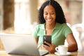 Happy black woman using phone and laptop in a bar Royalty Free Stock Photo