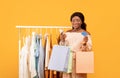 Happy black woman using smartphone for online shopping, standing near clothing rack with shopper bags and credit card Royalty Free Stock Photo