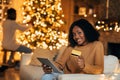 Happy black woman using tablet and credit card, ordering Xmas gifts on web, shopping for Christmas presents online Royalty Free Stock Photo