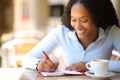 Happy black woman writing in agenda in a coffee shop terrace Royalty Free Stock Photo