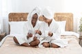 Happy black women with smartphone sitting on bed, drinking coffee Royalty Free Stock Photo