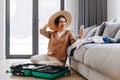 Happy blogger girl with a hat shows her followers how she is packing her suitcase for vacation. Relaxation concept Royalty Free Stock Photo