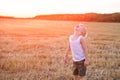 Happy blond boy stands with his head up on a mown wheat field. Sunset time Royalty Free Stock Photo